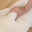 Close-up of a hand holding a fluffy white pillow on a wooden surface