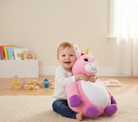 Child holding a pink unicorn plush toy in a room with toys and books on a shelf.