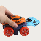 Toy car with large wheels held by a hand, with a second toy car in the background.